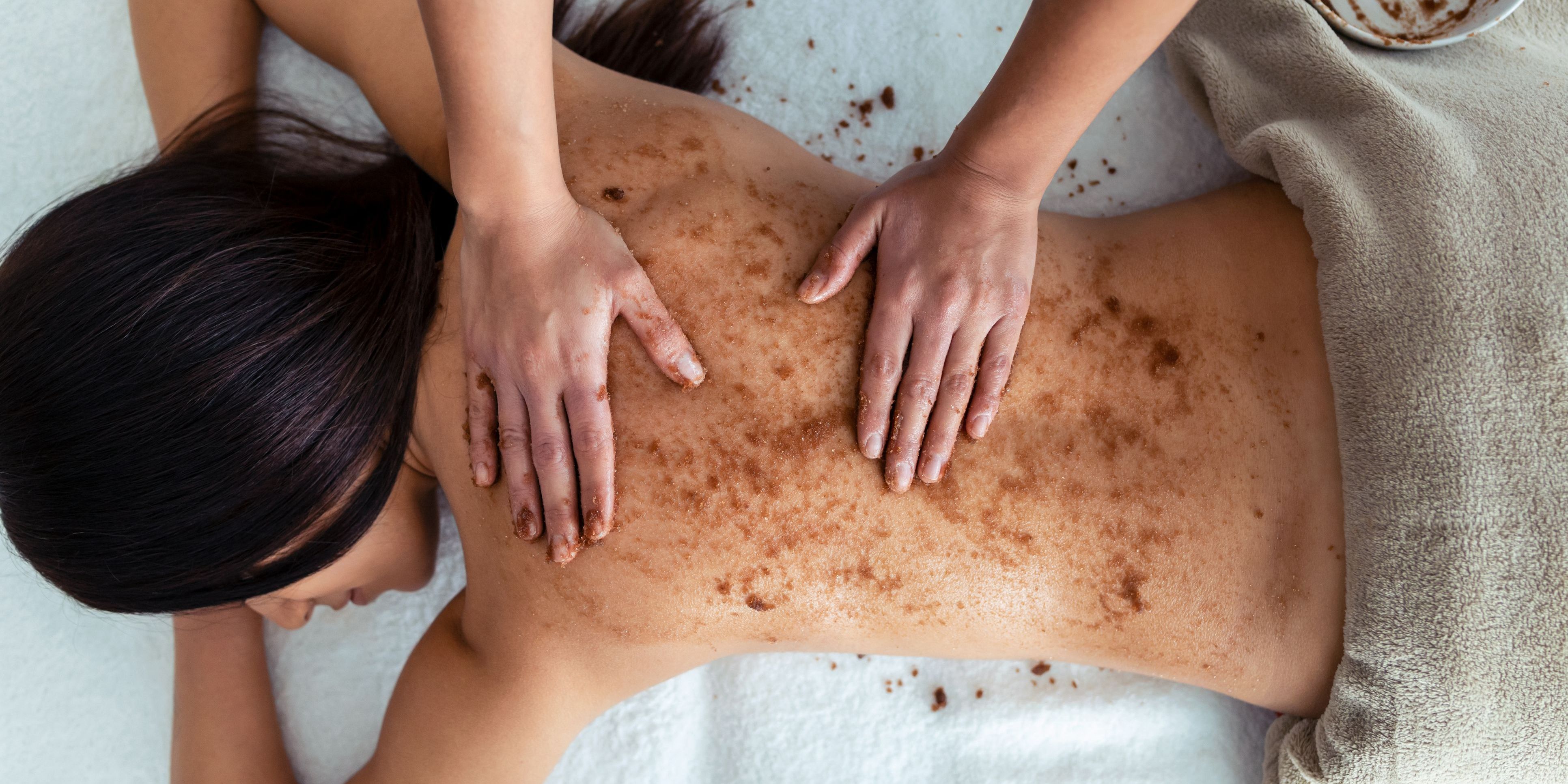 A body esthetician applying a scrub to a client's back.