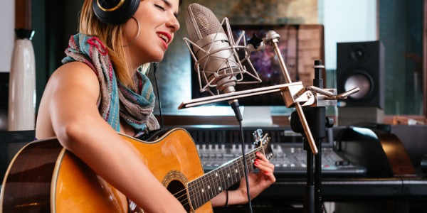 A music artist singing and playing guitar in a recording studio.