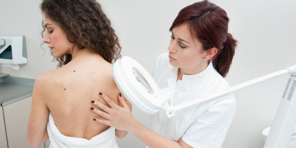 A dermatologist examining a patient's moles on their back.
