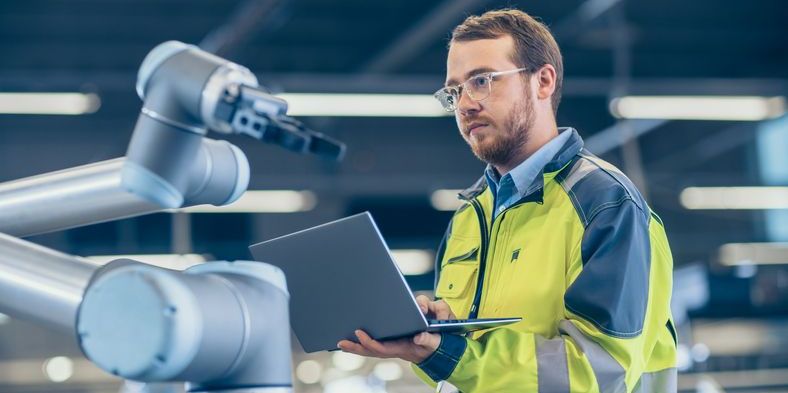 An automation engineer on the factory floor programming a robotic arm.